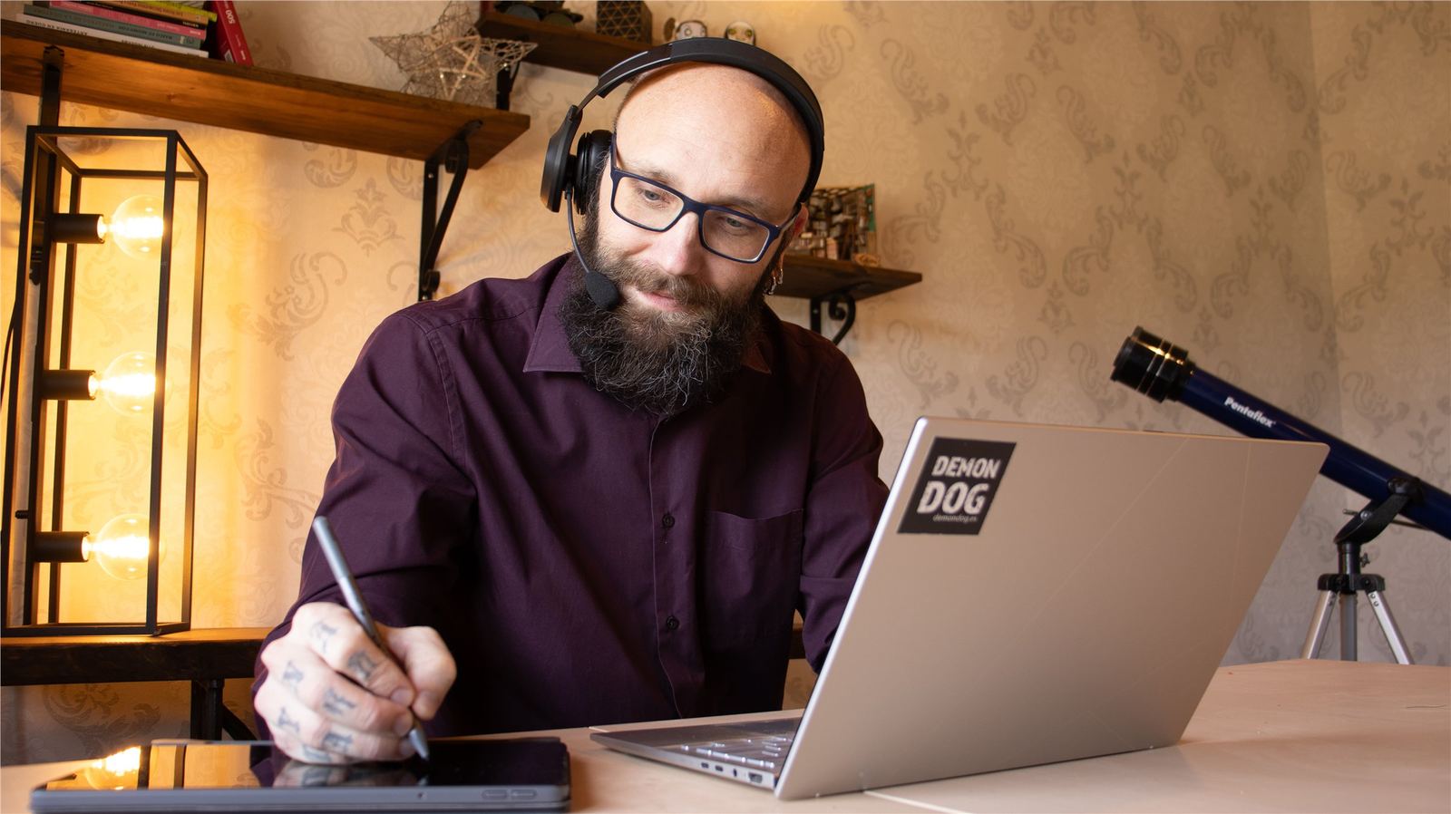 Björn working at a desk with a laptop, headset, drawing tablet, and warm studio light